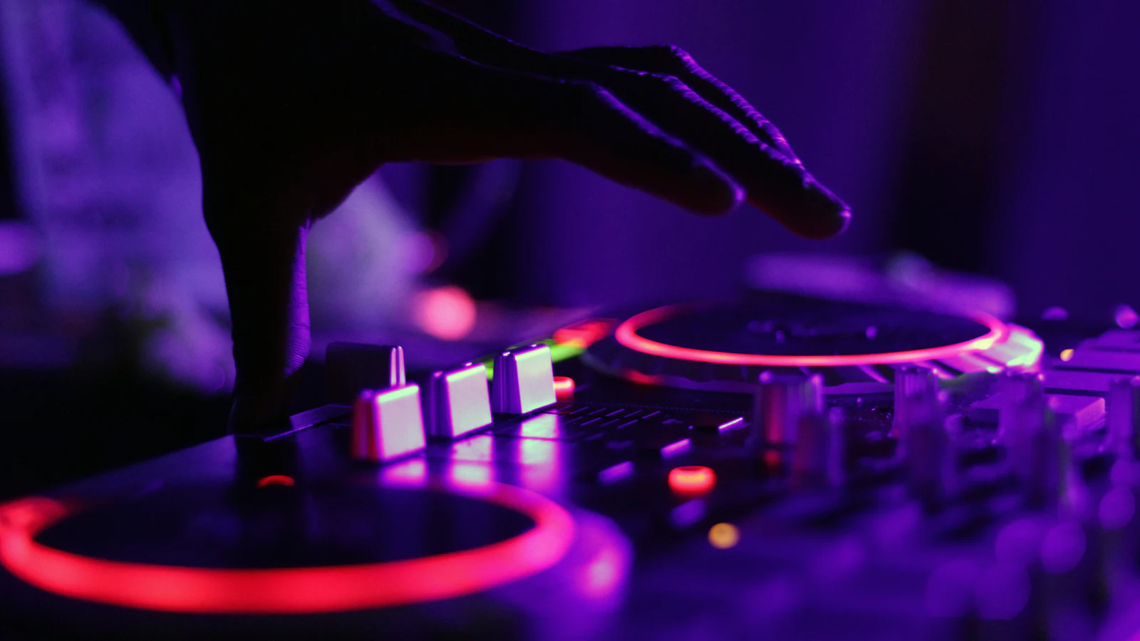 Les mains d'un DJ sur ses platines, sous une lumière violette